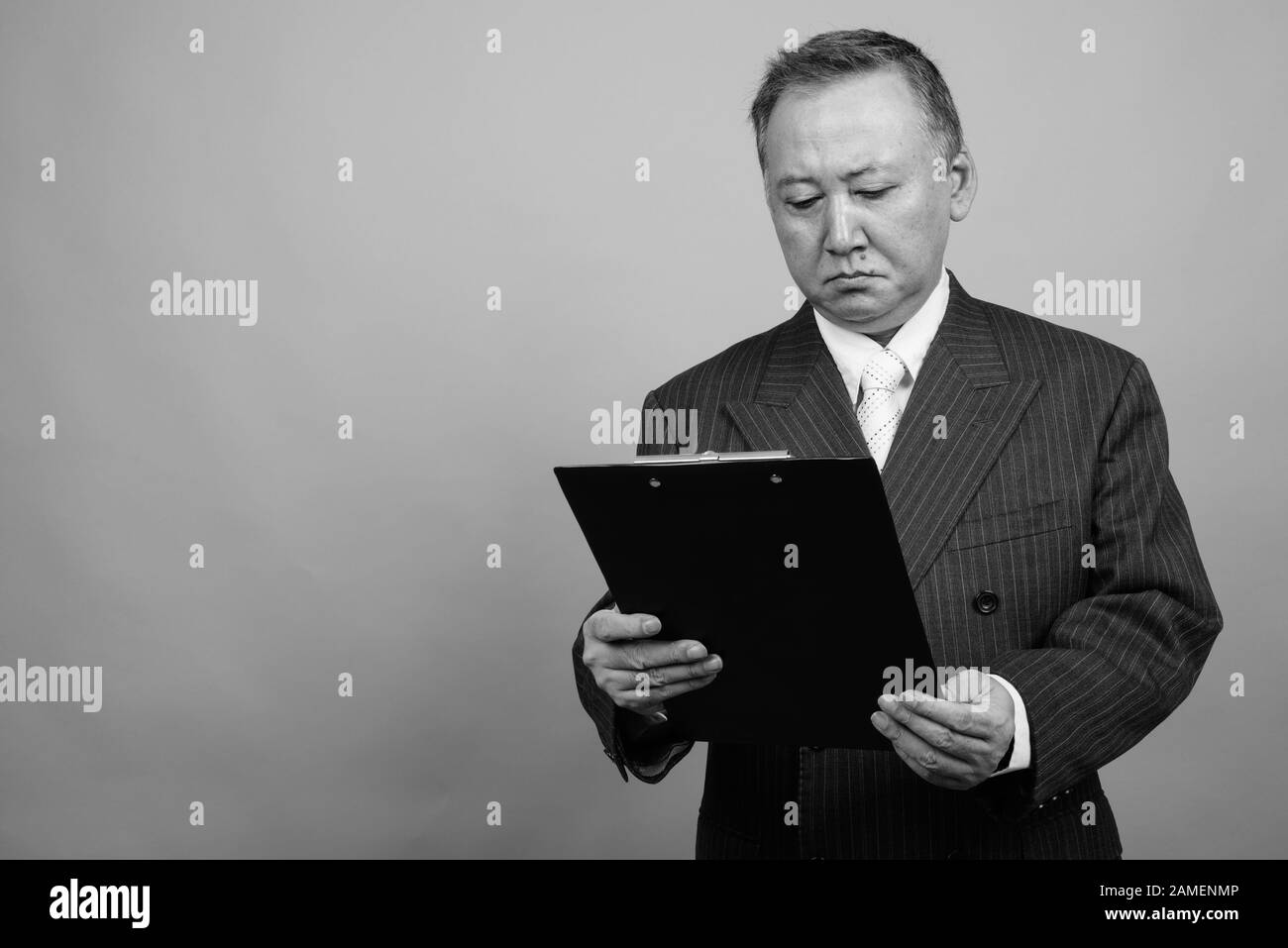 Studio shot of mature Asian businessman holding clipboard against gray ...