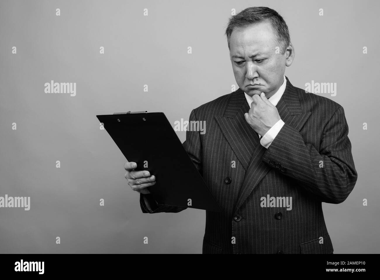 Studio shot of mature Asian businessman holding clipboard against gray ...