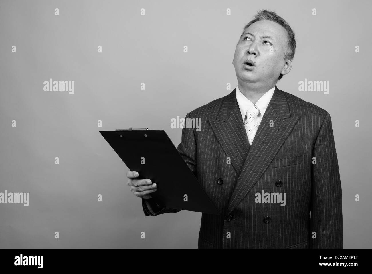 Studio shot of mature Asian businessman holding clipboard against gray ...