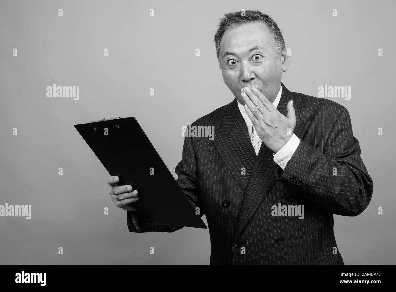Studio shot of mature Asian businessman holding clipboard against gray ...