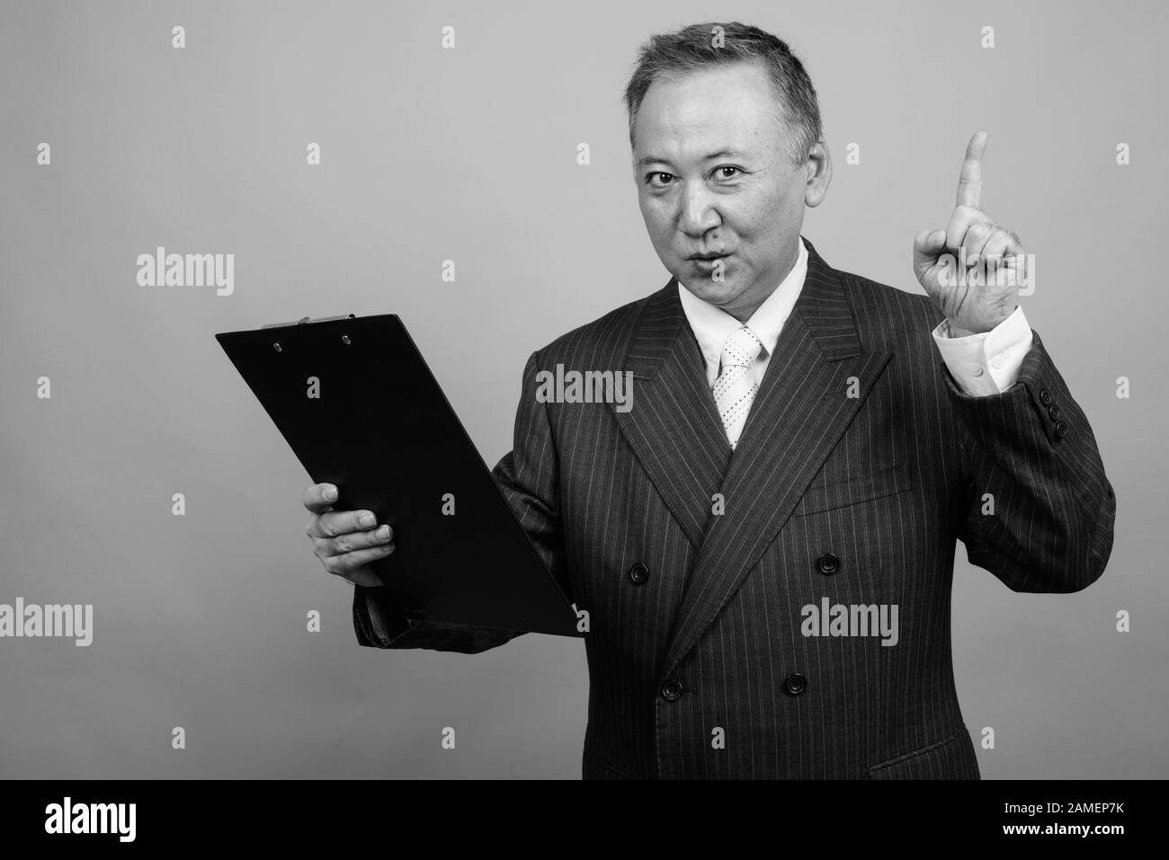 Studio shot of mature Asian businessman holding clipboard against gray ...