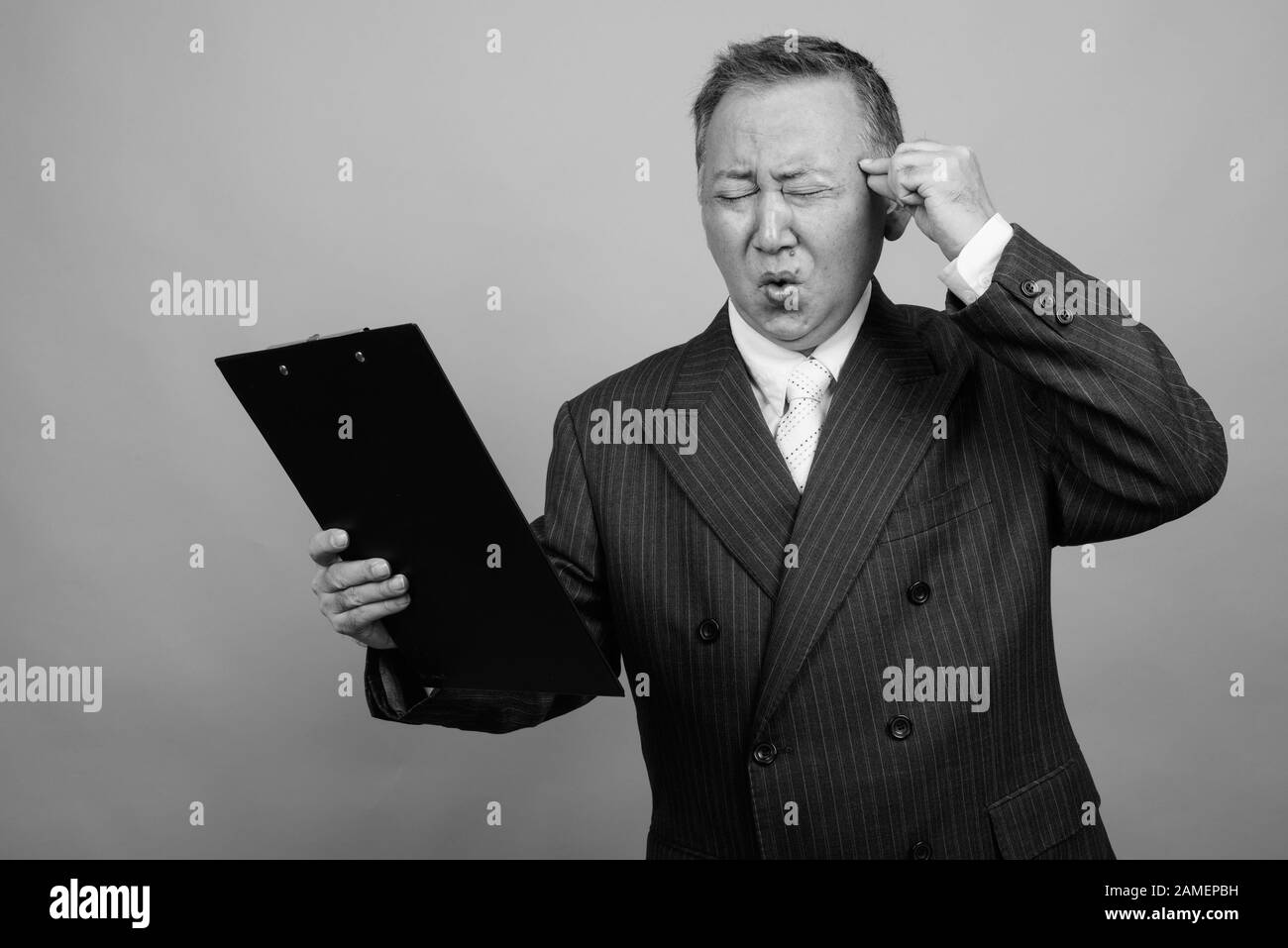 Studio shot of mature Asian businessman holding clipboard against gray ...