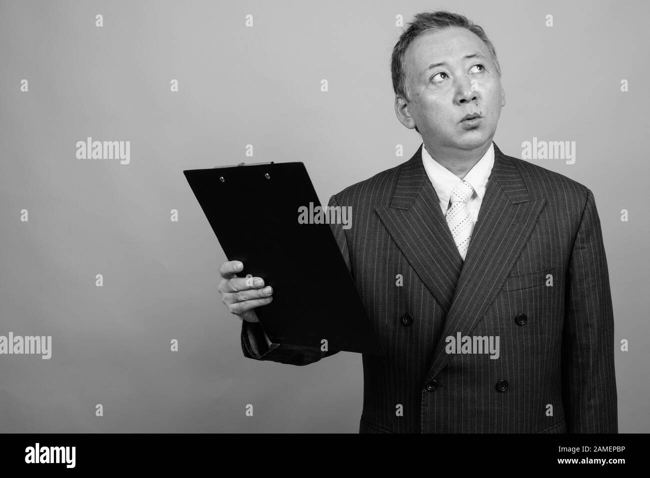 Studio shot of mature Asian businessman holding clipboard against gray ...