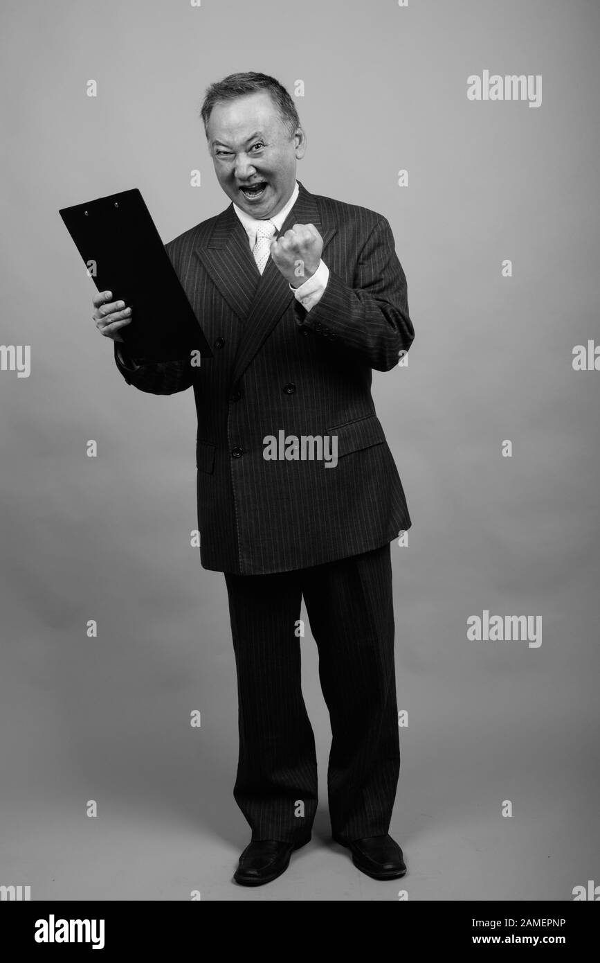 Studio shot of mature Asian businessman holding clipboard against gray ...