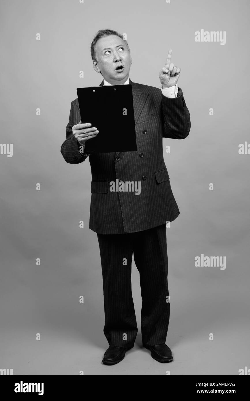 Studio shot of mature Asian businessman holding clipboard against gray ...
