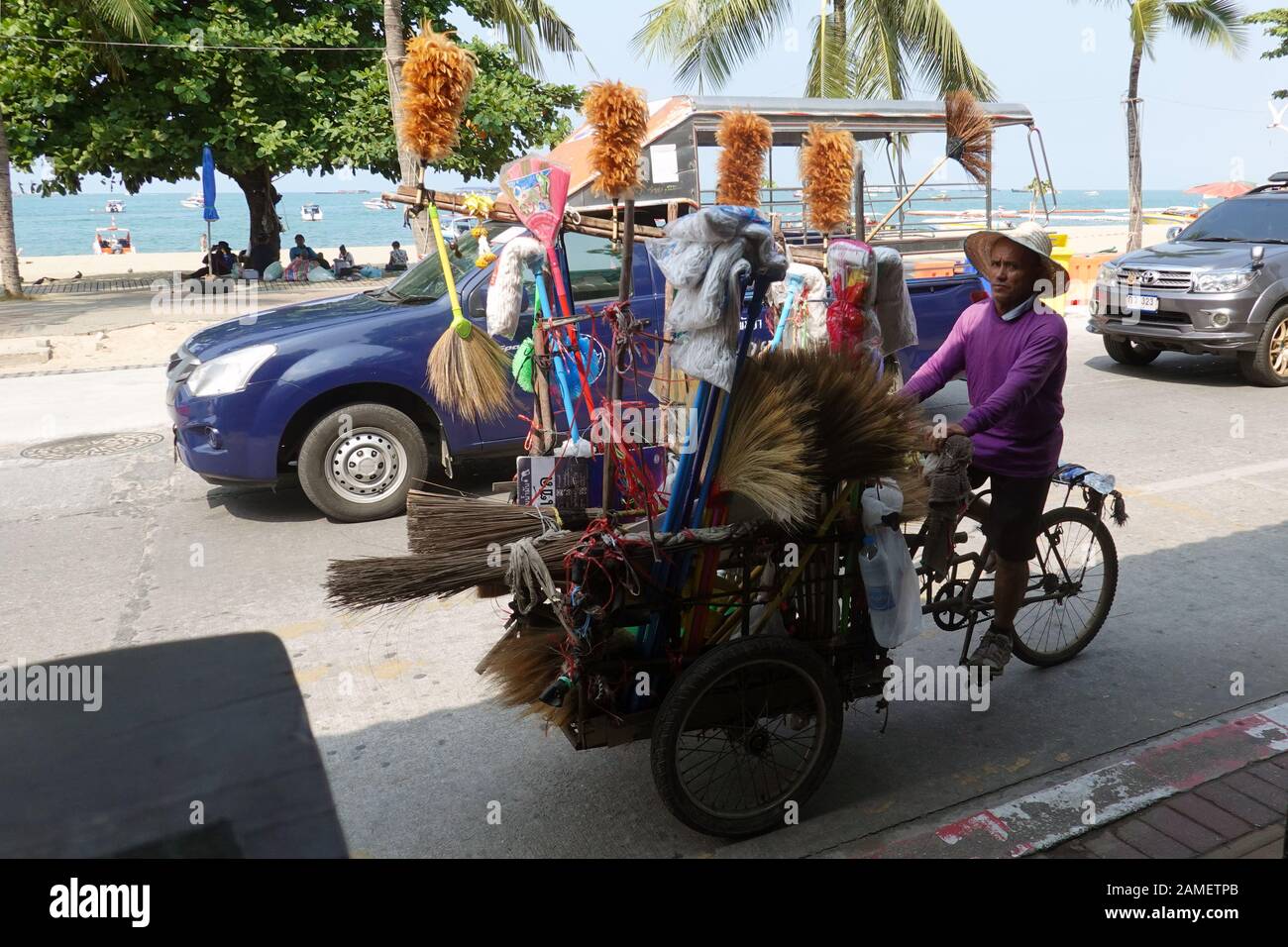 Pattaya, Thailand - December 24, 2019: Cleaning equipment seller. Man riding bicycle cart with all kind of brushes on Beach Road. Stock Photo