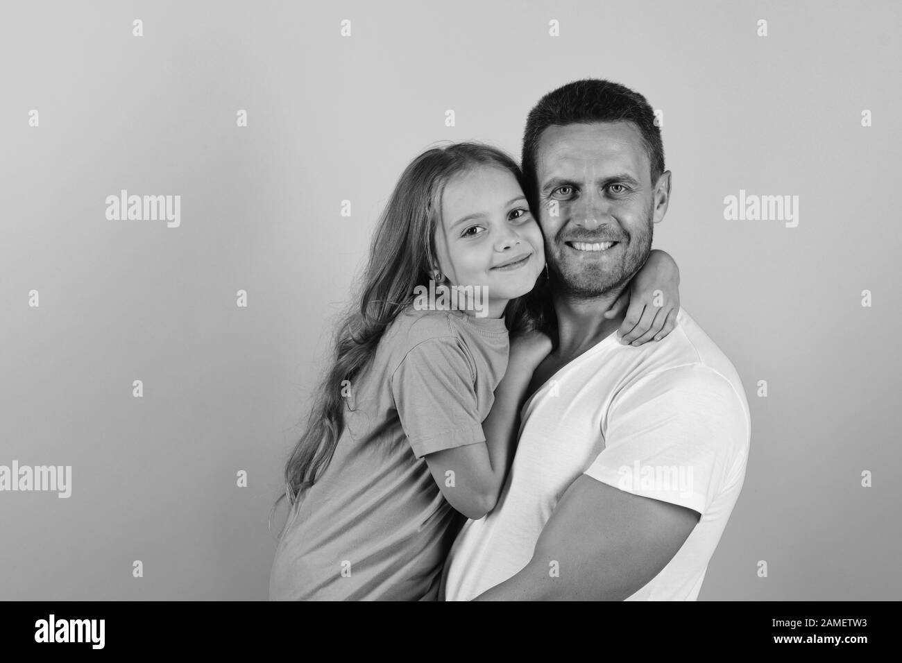 Daughter and father hug each other. Girl and man with happy faces isolated on blue background. Childhood and family concept. Schoolgirl and dads pose cheek to cheek, copy space. Stock Photo