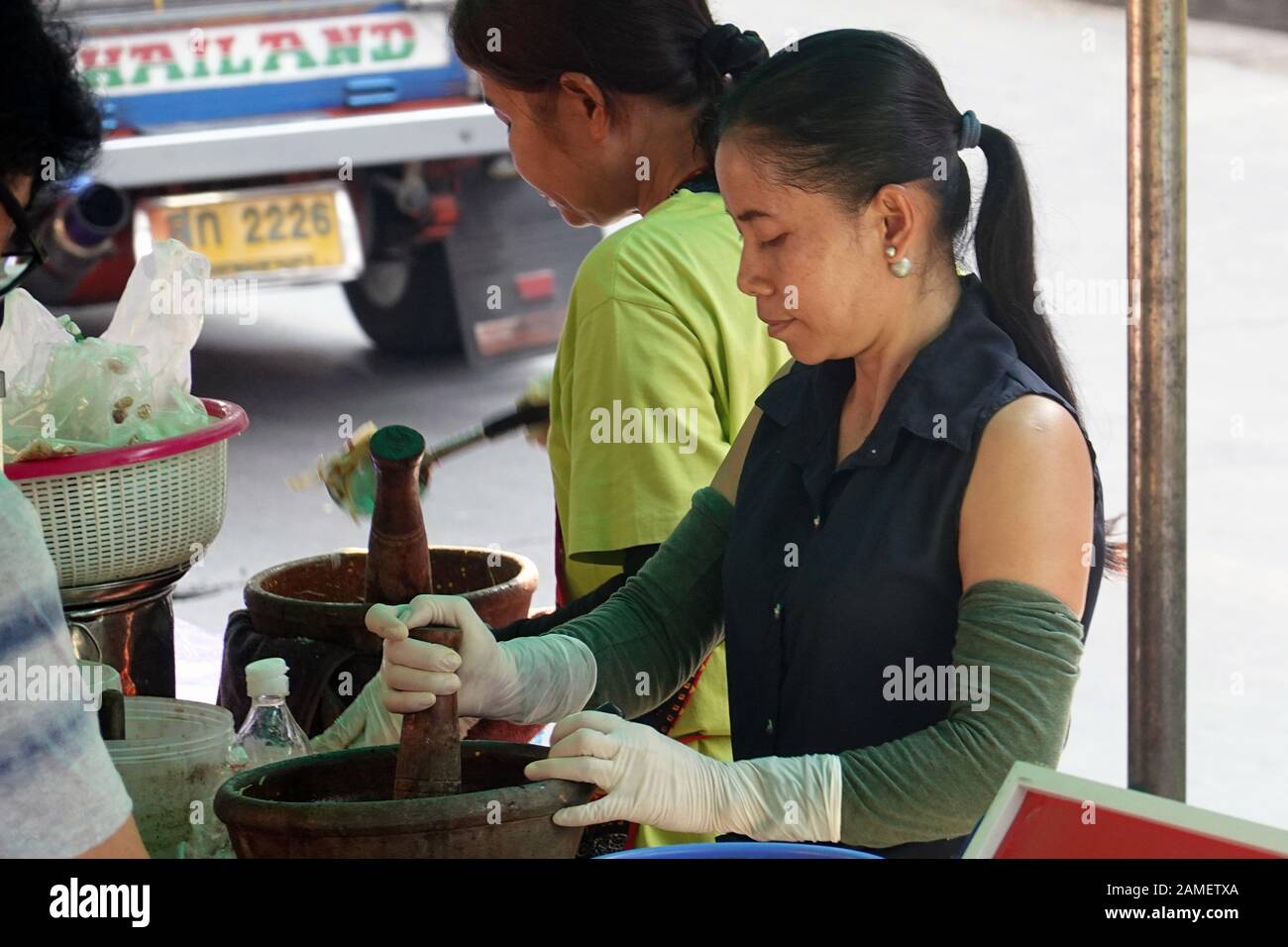 Bangkok, Thailand - December 26, 2019:  Street vendor woman using a big mortar and pestle and making Som tam, a green papaya salad. Stock Photo