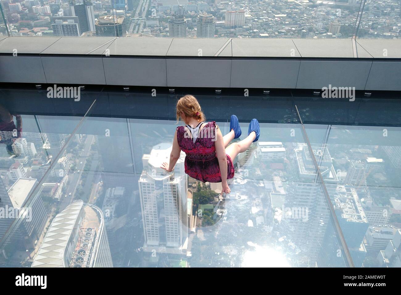Bangkok, Thailand - December 21, 2019: Woman sitting on glass floor on rooftop of the King Power Mahanakhon building and looking down through glass. Stock Photo