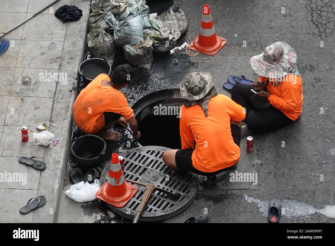 Bangkok, Thailand - December 21, 2019: Workers cleaning sewer with buckets and scoop net to waste bags. One worker using a phone. Stock Photo