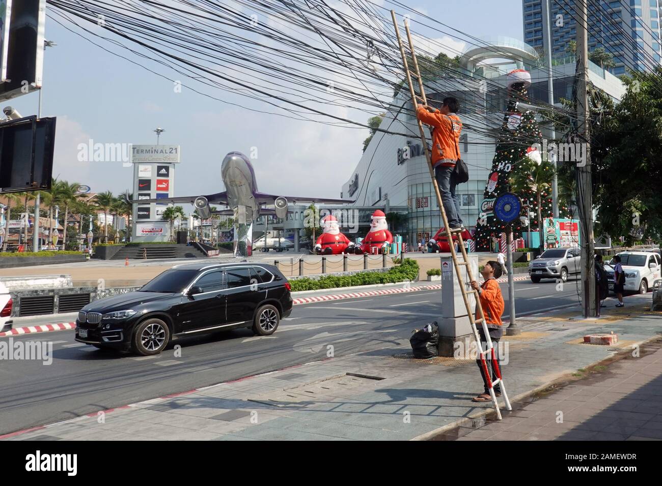 Pattaya, Thailand - December 23, 2019: Workers. Man on a bamboo ladder leans against the power line. Other man holds ladder. Stock Photo