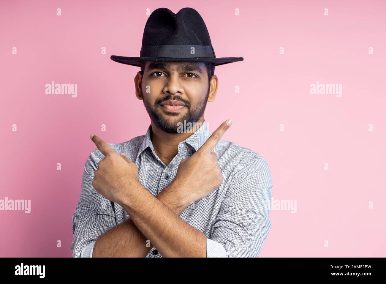 Close up shot of pleased handsome young unshaven indian man wearing casual  shirt, stylish black hat, looking at camera and pointing with forefingers i  Stock Photo - Alamy