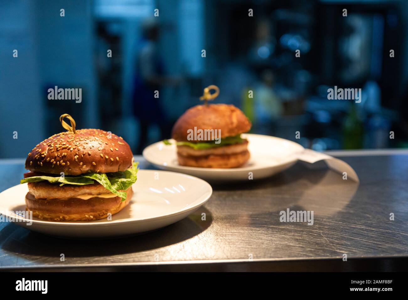 Ready meals hamburgers at the counter for delivery to waiters in a restaurant and kitchen in the background. Stock Photo