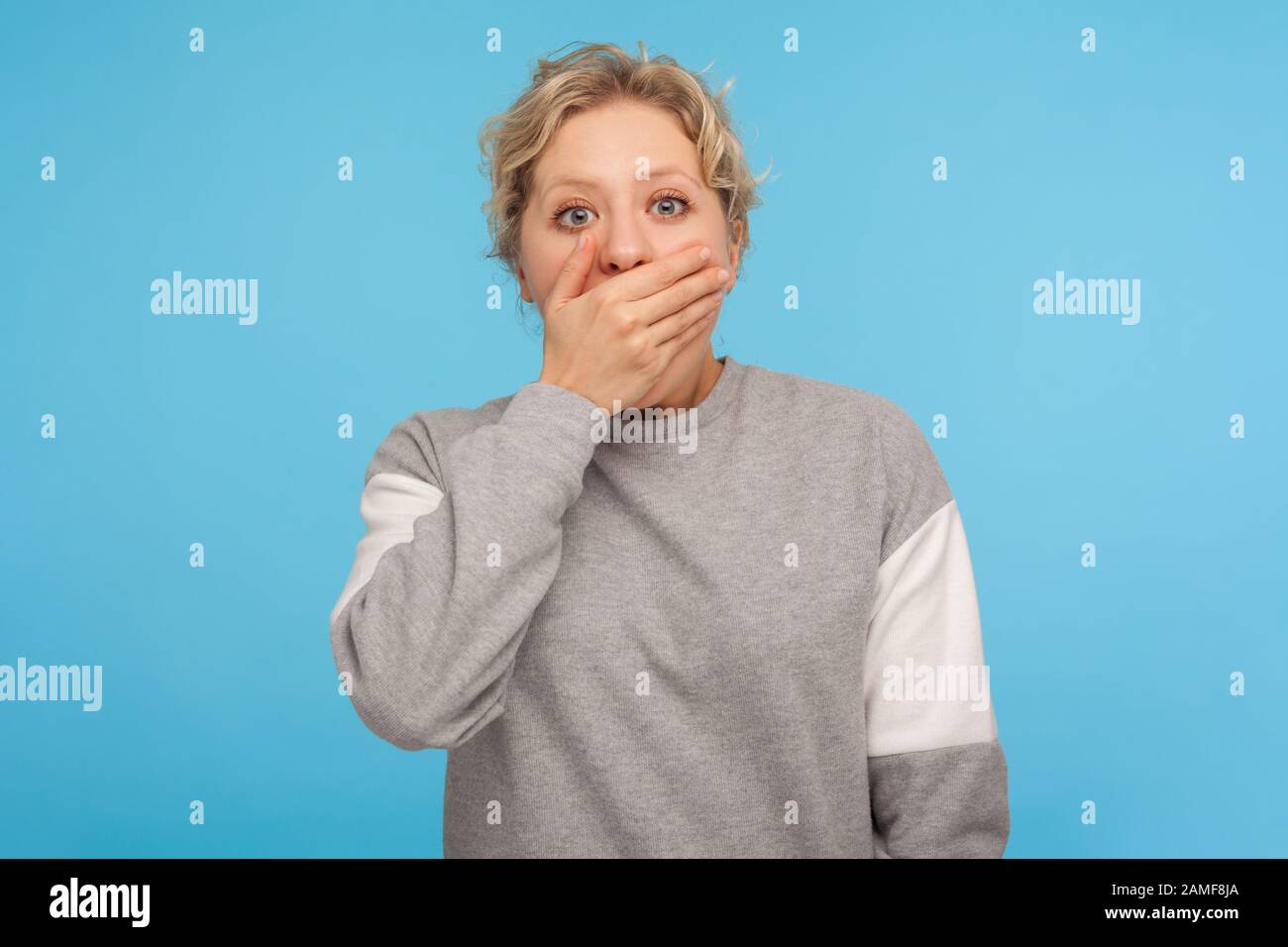 I won't tell! Shocked intimidated woman in grey sweatshirt covering mouth with hand and looking scared at camera, bullied victim silent about truth. i Stock Photo