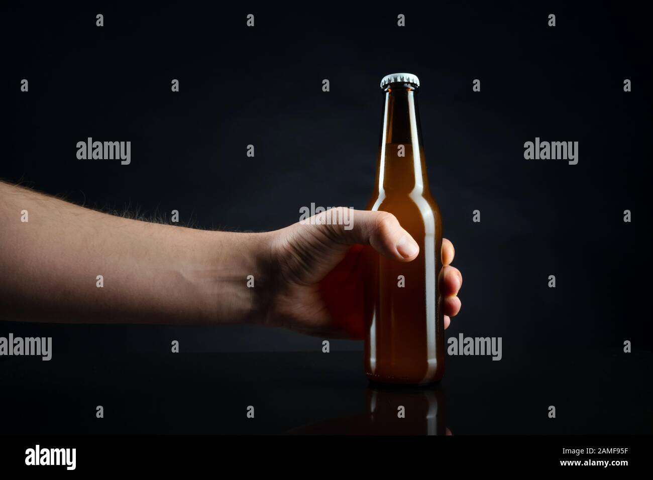 Men holding cold unopened bottle of beer with cap on black background