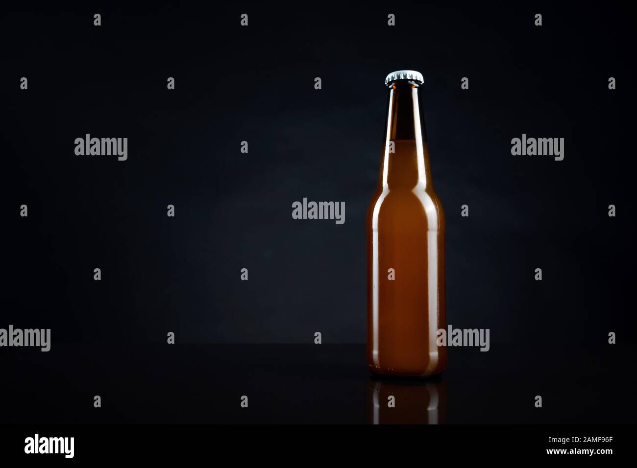 Cold unopened bottle of beer with cap on black background. Glass of