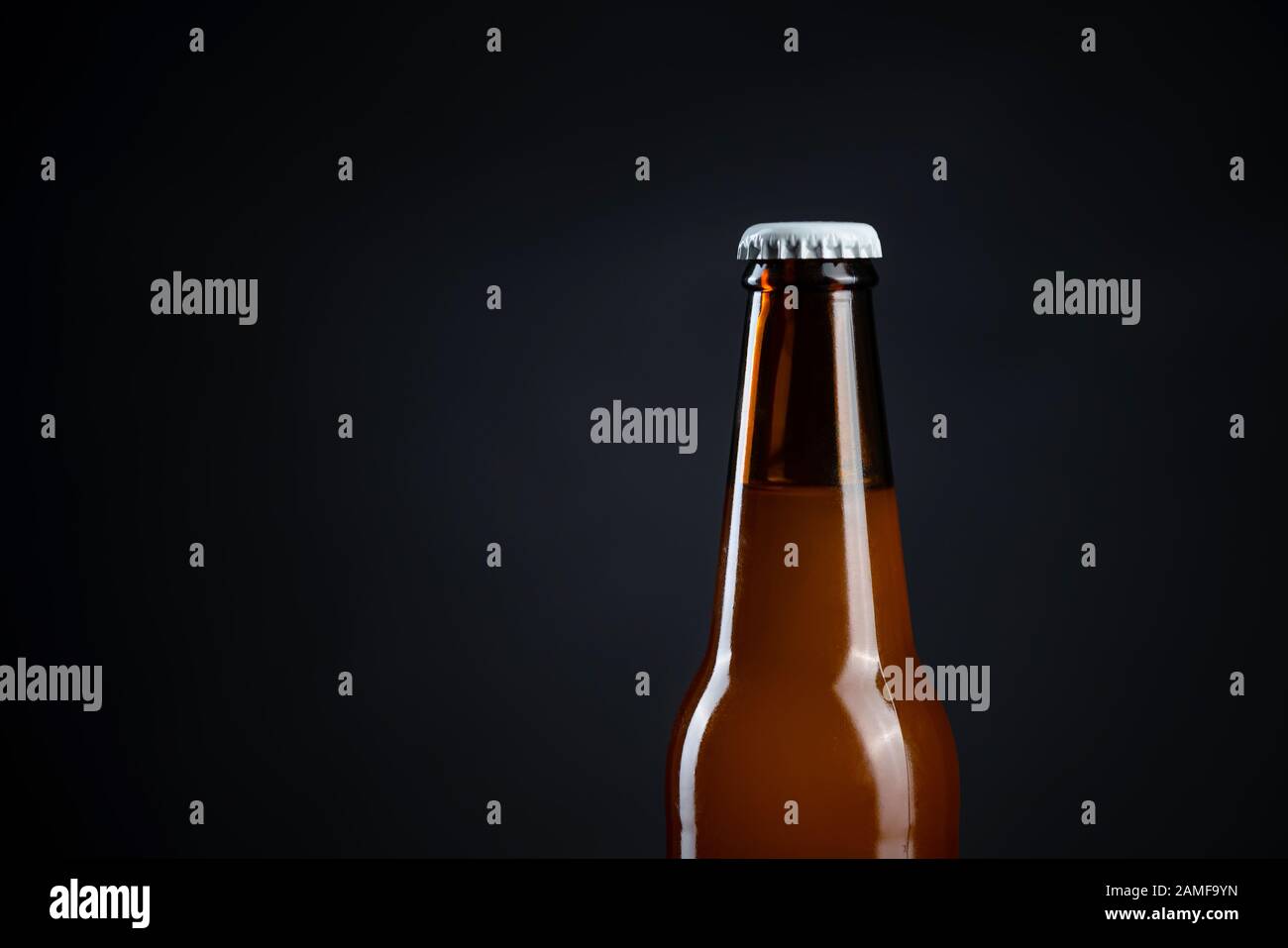 Cold unopened bottle of beer with cap on black background. Glass of