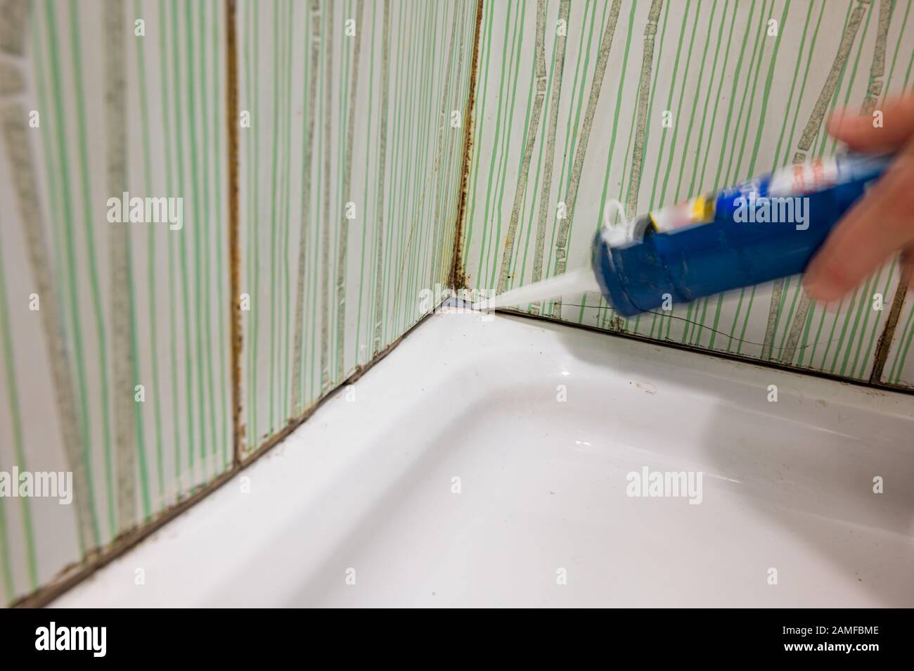 Fixing old mold destroy join lines in bathroom with caulking gun Stock