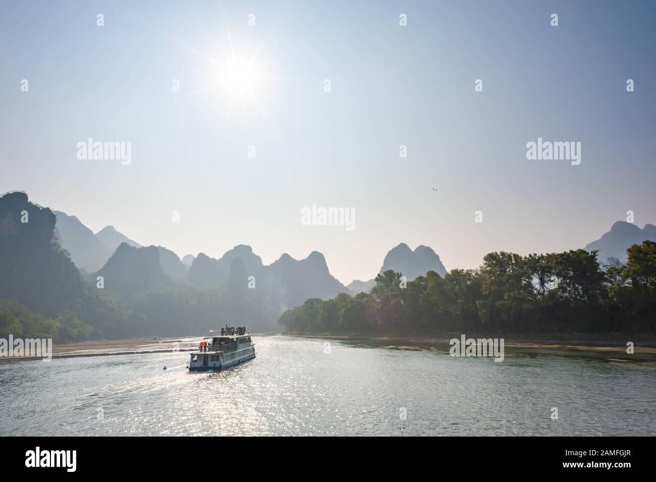 Boat on Li river cruise against the sun and karst formation mountain landscape in the fog between Guiling and Yangshuo, Guangxi province, China Stock Photo
