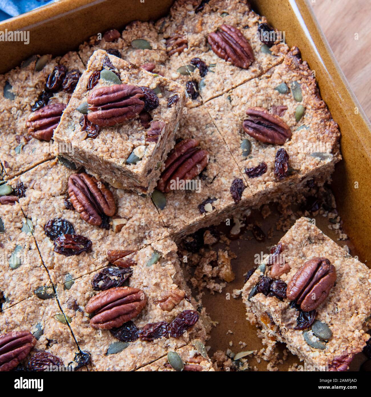 over head square shot of cut Plant based vegan cake in a brown oven dish ,recipe filled with nuts fruit and oats copy space in background Stock Photo