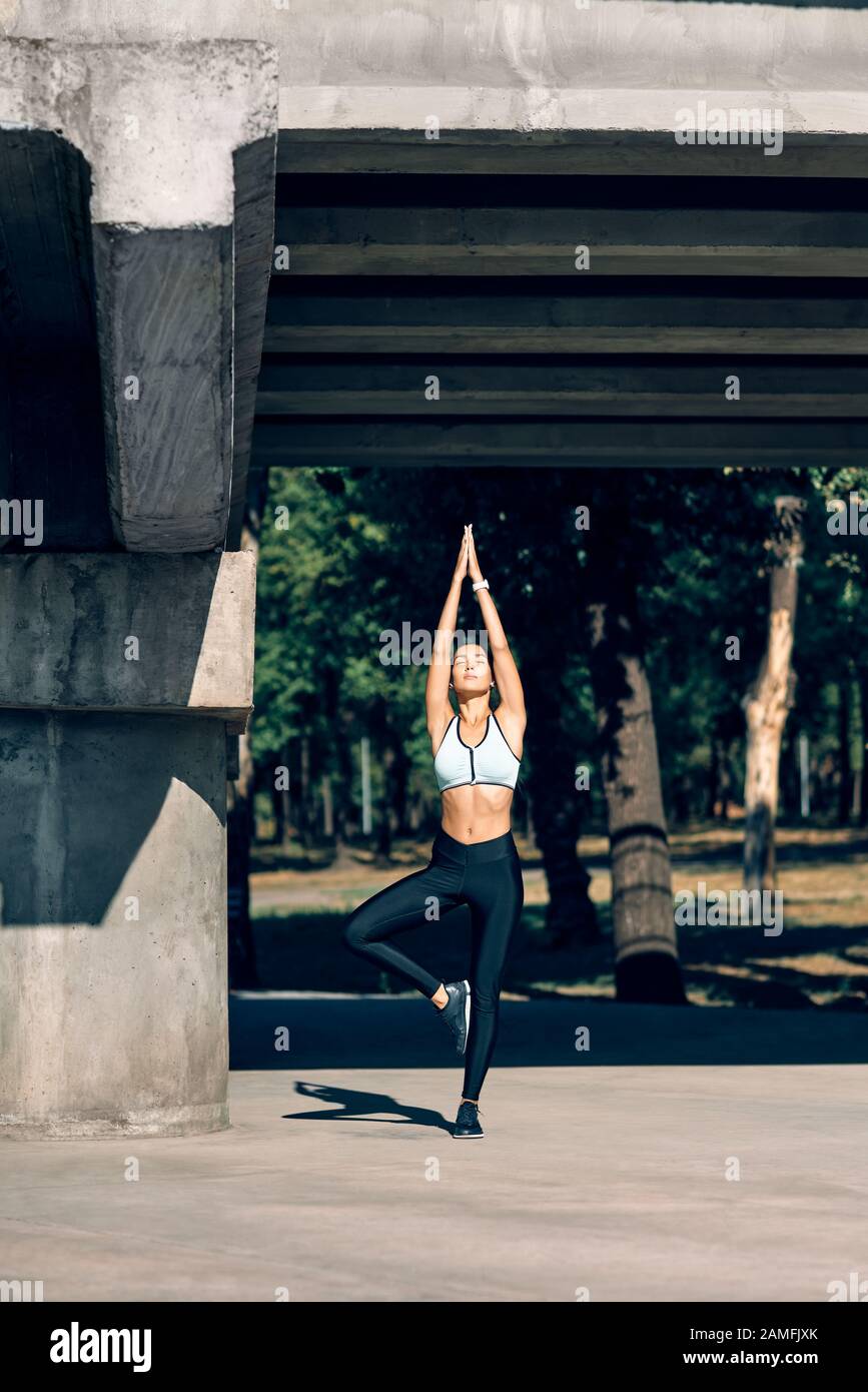 Young sporty woman doing yoga exercise Tree Pose asana outdoors ...