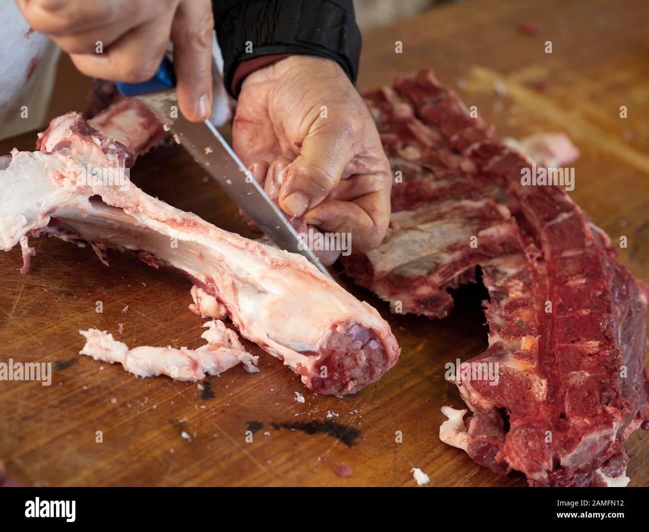 Pork butchery, traditional rustic style. Removing as much meat as possible from bones, avoiding waste. Stock Photo