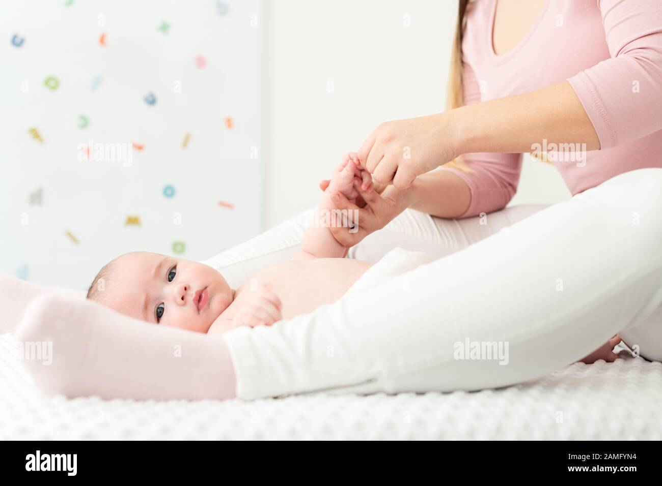 Baby massage background. Mother gently massaging her baby boy. Baby lying on back and looking at camera during massage. Stock Photo