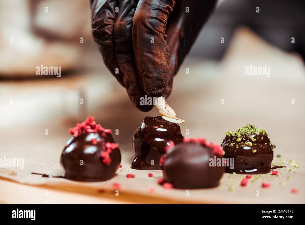 cropped view of chocolatier in black latex glove adding nuts on fresh made candies Stock Photo