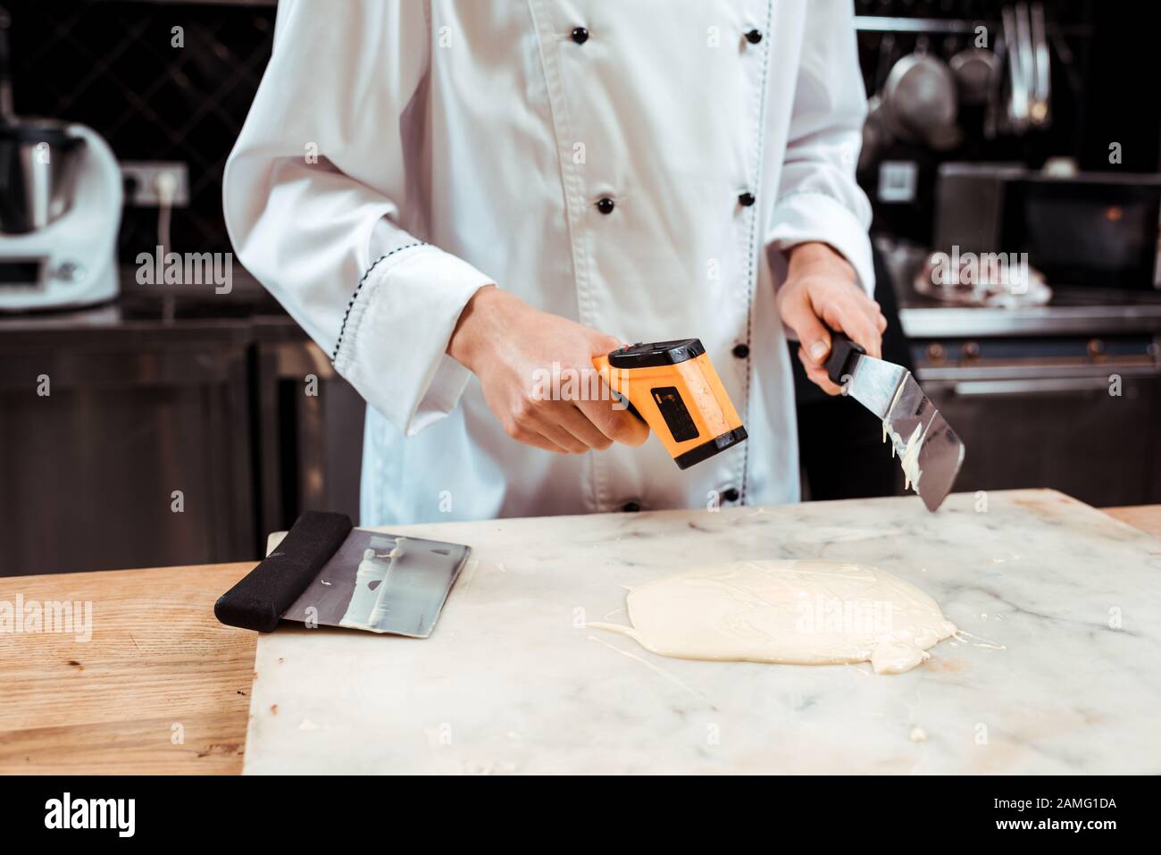 cropped view of chocolatier measuring temperature of melted white ...