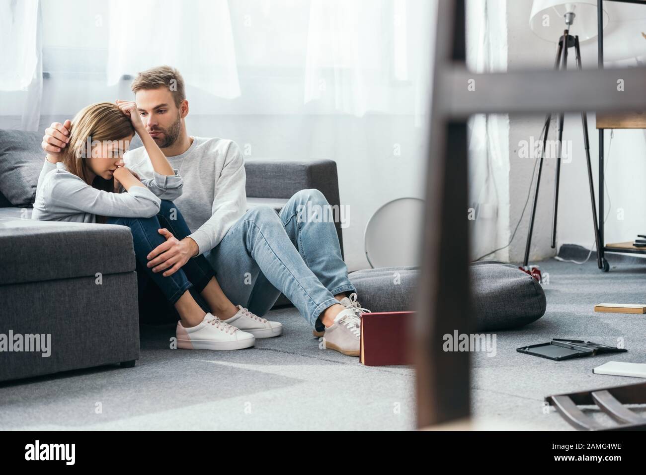 handsome man calming down sad woman in robbed apartment Stock Photo
