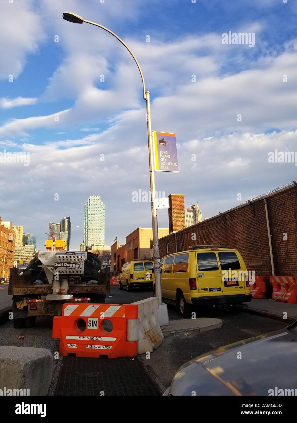 View facing east along 44th Drive from Anable Basin, in Hunters Point, Long Island City, Queens, March 11, 2019. NYC Dept of Transportation vehicles and construction equipment clutter the road.   At center is a 1970s-era Westinghouse lamp post with a 1990s-era sign advertising the 'Long Island City Industrial Park'. Citigroup Building at One Court Square in the background. Ecommerce retailer Amazon has planned to locate a major regional headquarters in this area. () Stock Photo