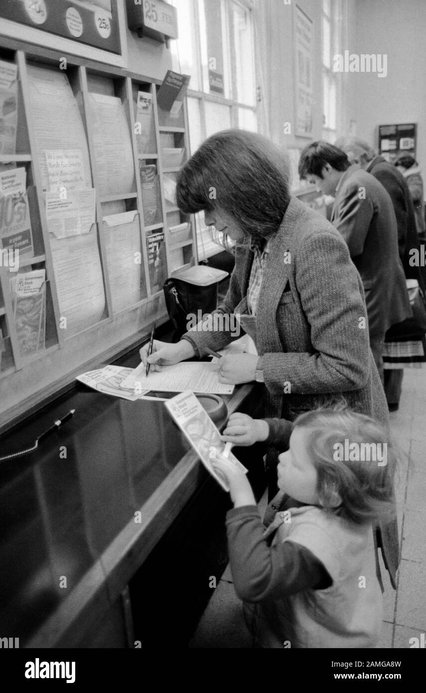 Post Office 1980s London UK. People filling in forms selecting leaflets. Mother and child going to the Post Office 1981 HOMER SYKES Stock Photo
