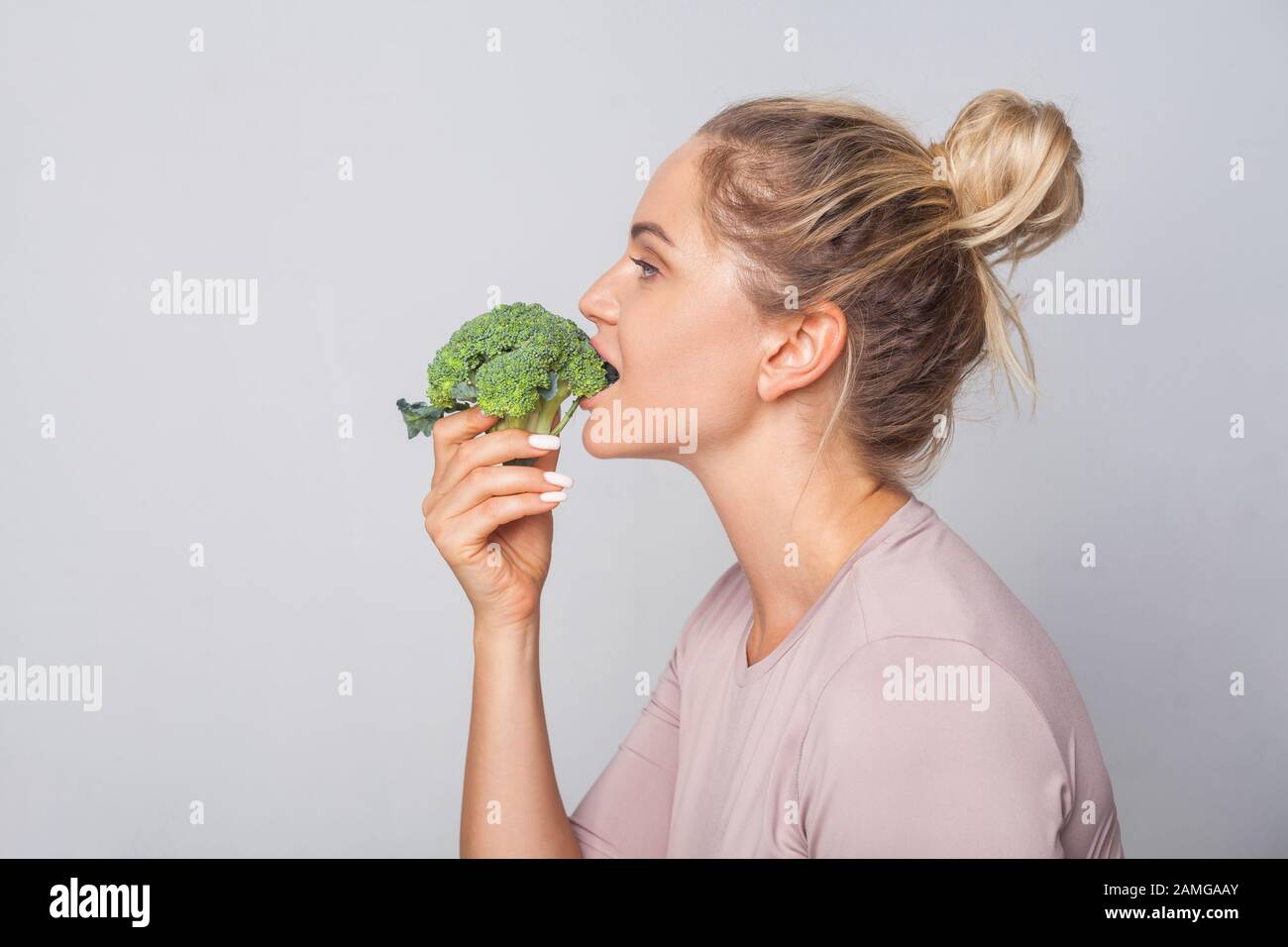 Side view of attractive young woman with hair bun biting green broccoli,  eating fresh vegetable, enjoying healthy food, vegetarian diet, nutrition.  in Stock Photo - Alamy