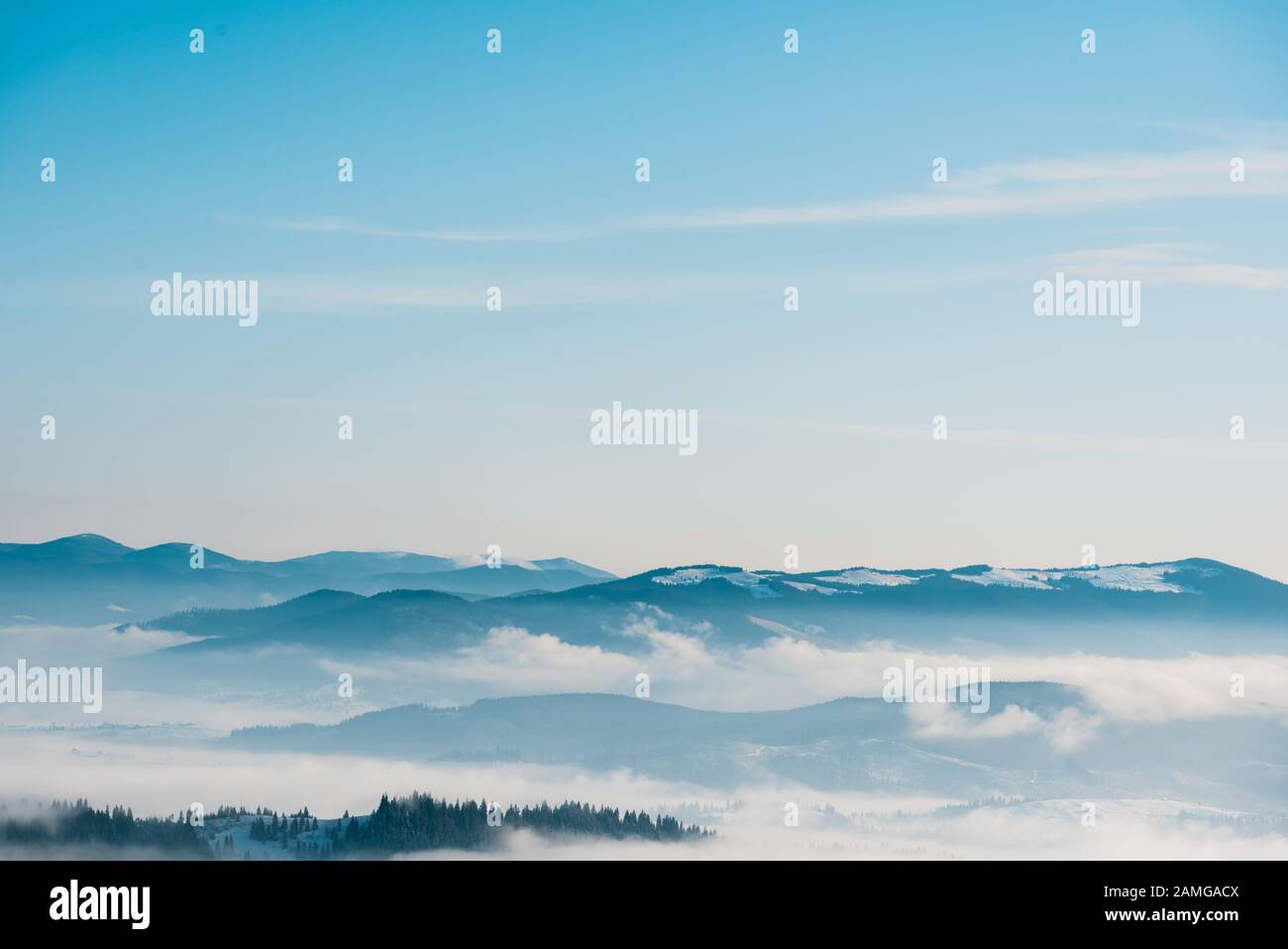 scenic view of snowy mountains with pine trees in white fluffy clouds ...