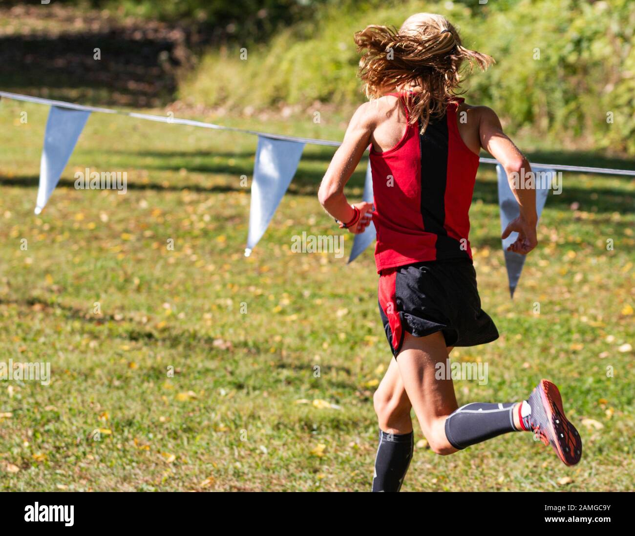Rear view of a female high school cross country runner racing on the grass at the New York State Federation course in Bowdoin park. Stock Photo
