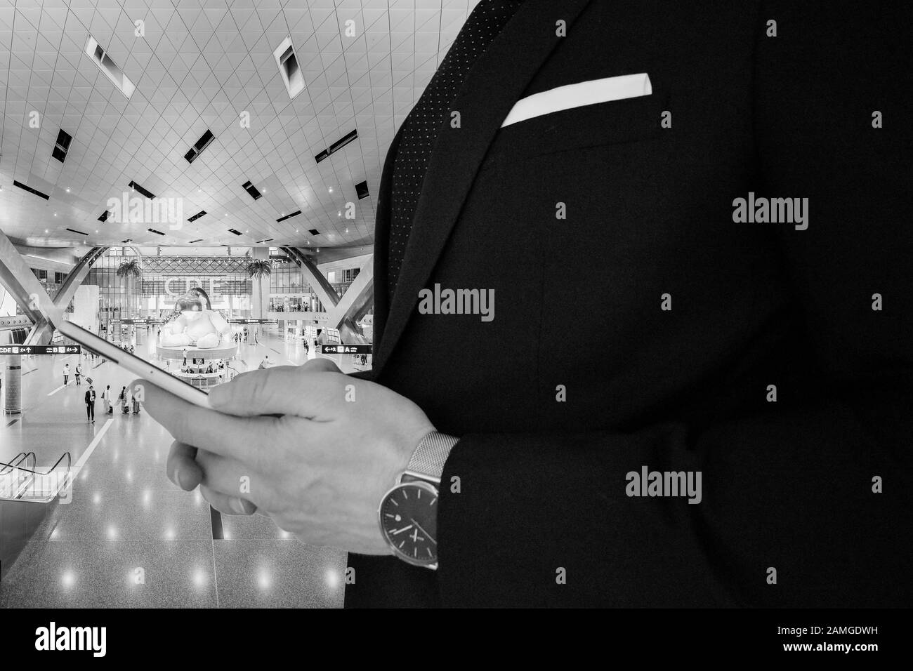 A close up view of a business man in a black suit holding a smartphone in a train station Stock Photo