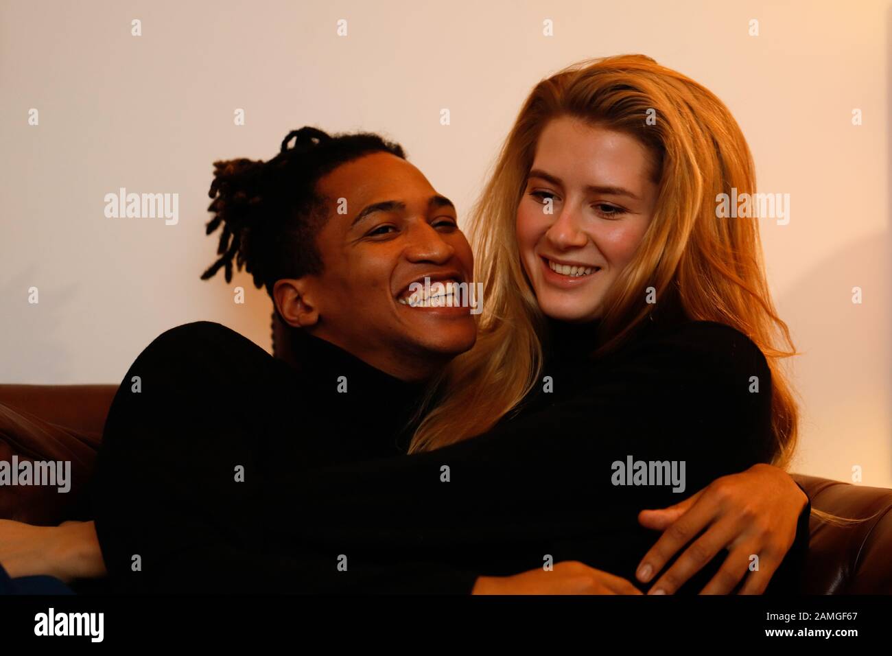 Young intercultural caucasian-hispanic student couple posing on sofa. Stock Photo