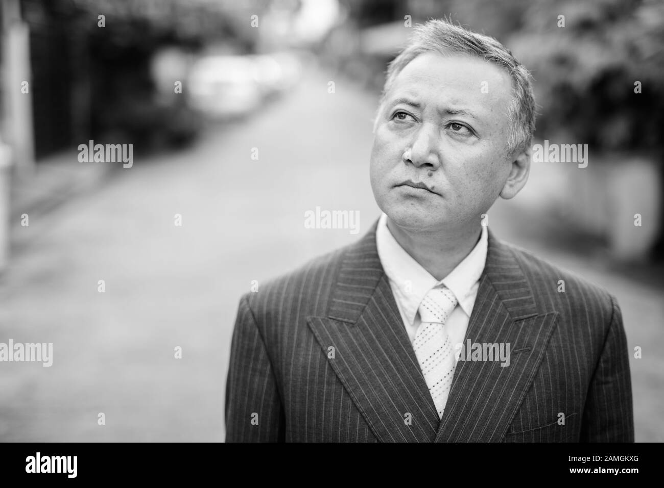 Portrait of mature Asian businessman wearing suit in the streets ...