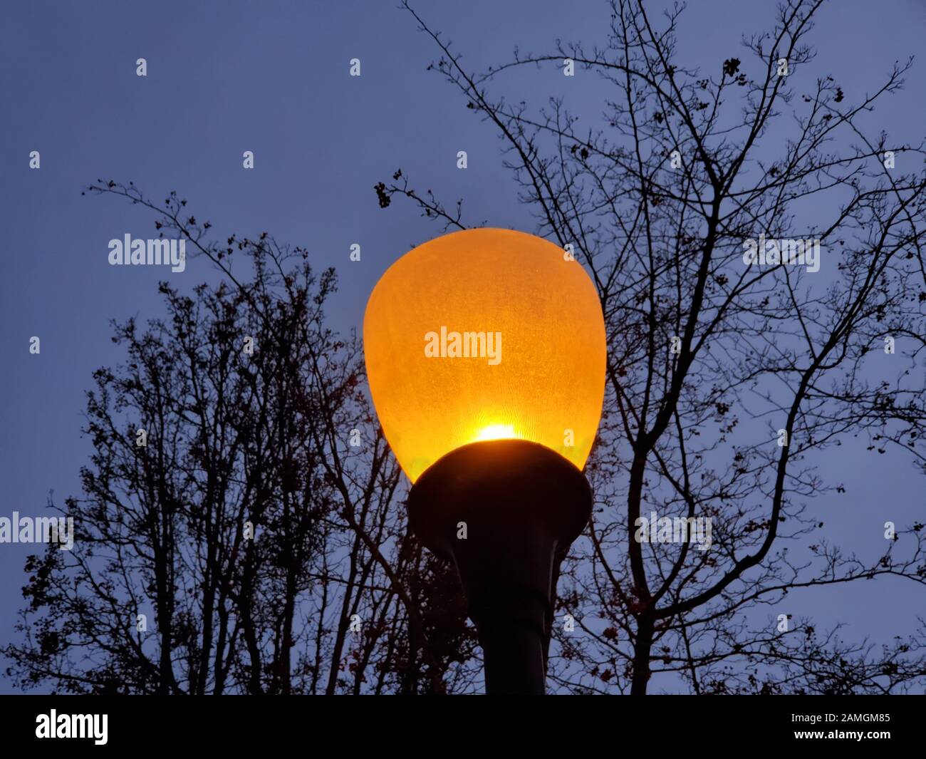 Close-up up top of street lamp, showing typical orange glow of a sodium vapor light, San Ramon, California, December 18, 2019. As more areas switch to LED street lighting, the color temperature of nightime lights is increasing, from the dark yellow of sodium vapor lamps to the bright white of LEDs. () Stock Photo