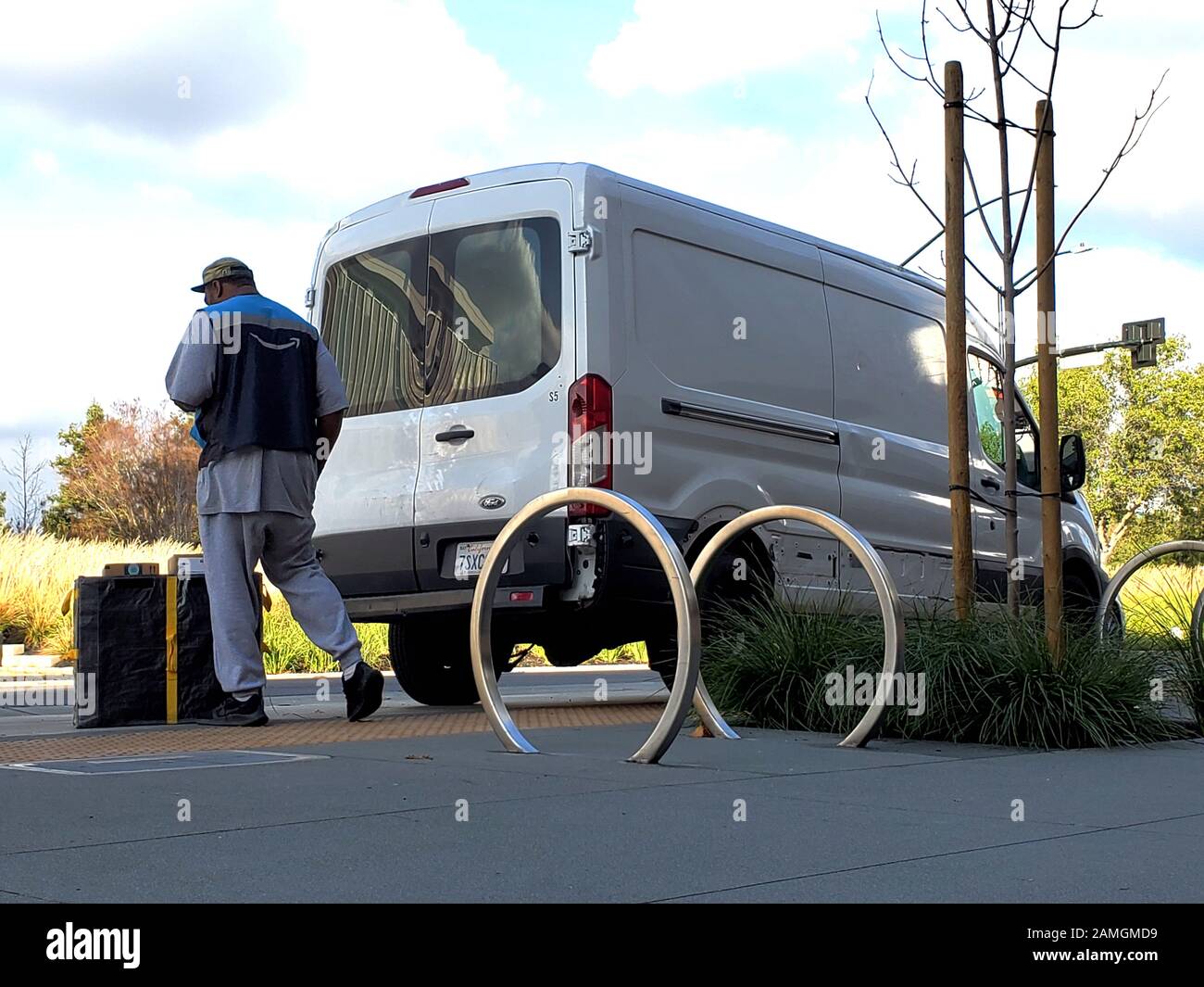 Low-angle view of a delivery worker wearing a vest with the Amazon logo unloading packages for delivery from a white unmarked van at an office park in San Ramon, California, December 19, 2019. () Stock Photo