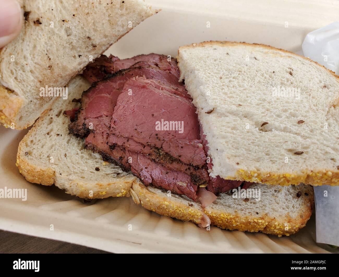 Closeup of pastrami sandwich on rye bread in takeout container at Wise