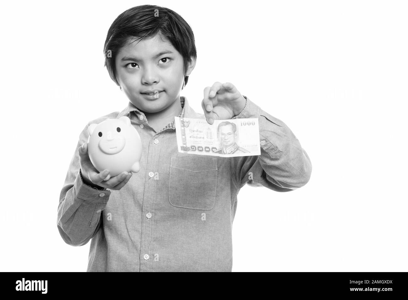 Thoughtful Japanese boy holding piggy bank and 1000 thai baht Stock Photo