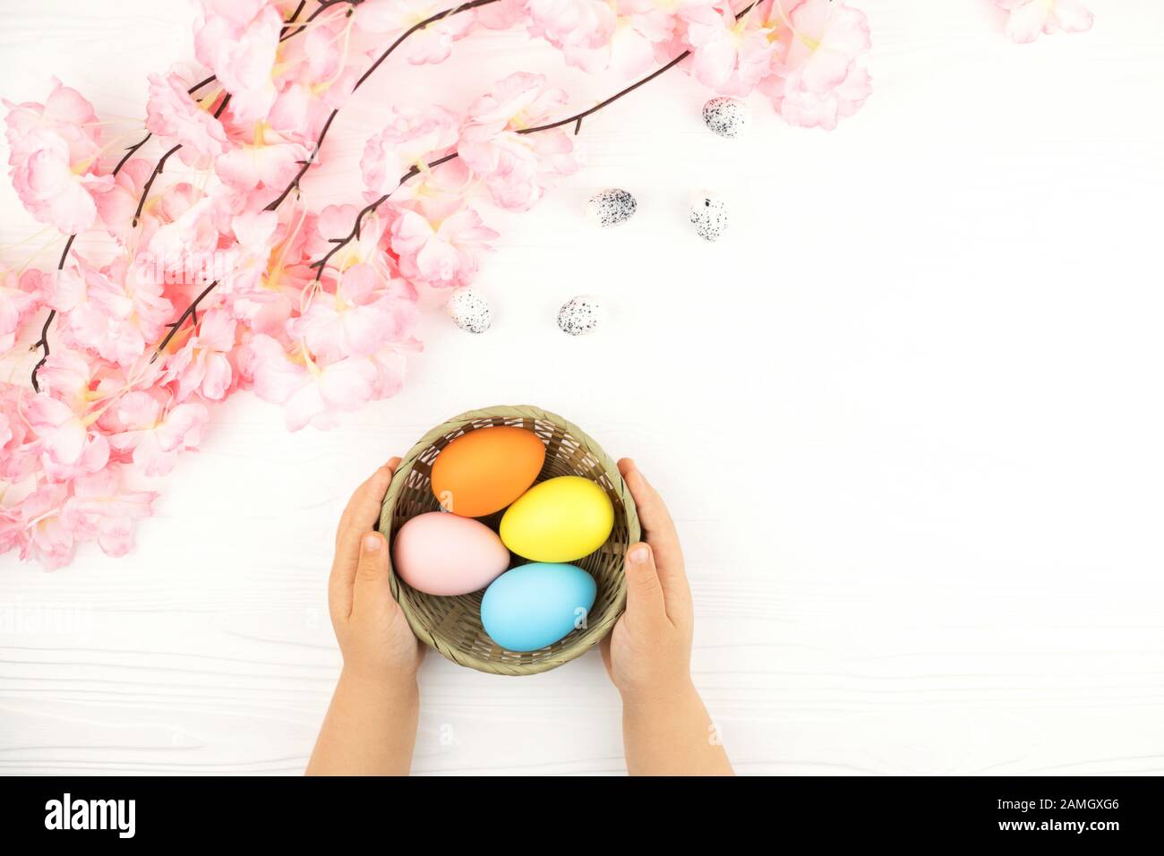 Child's hands holding basket with colored eggs on the Easter background. Stock Photo