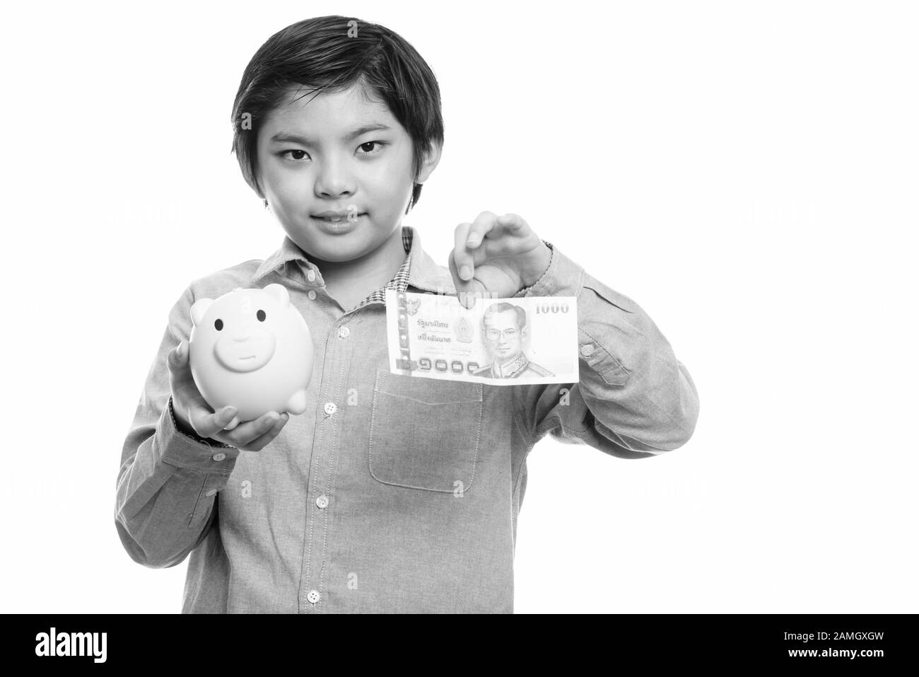 Studio shot of cute Japanese boy holding piggy bank and 1000 thai baht Stock Photo
