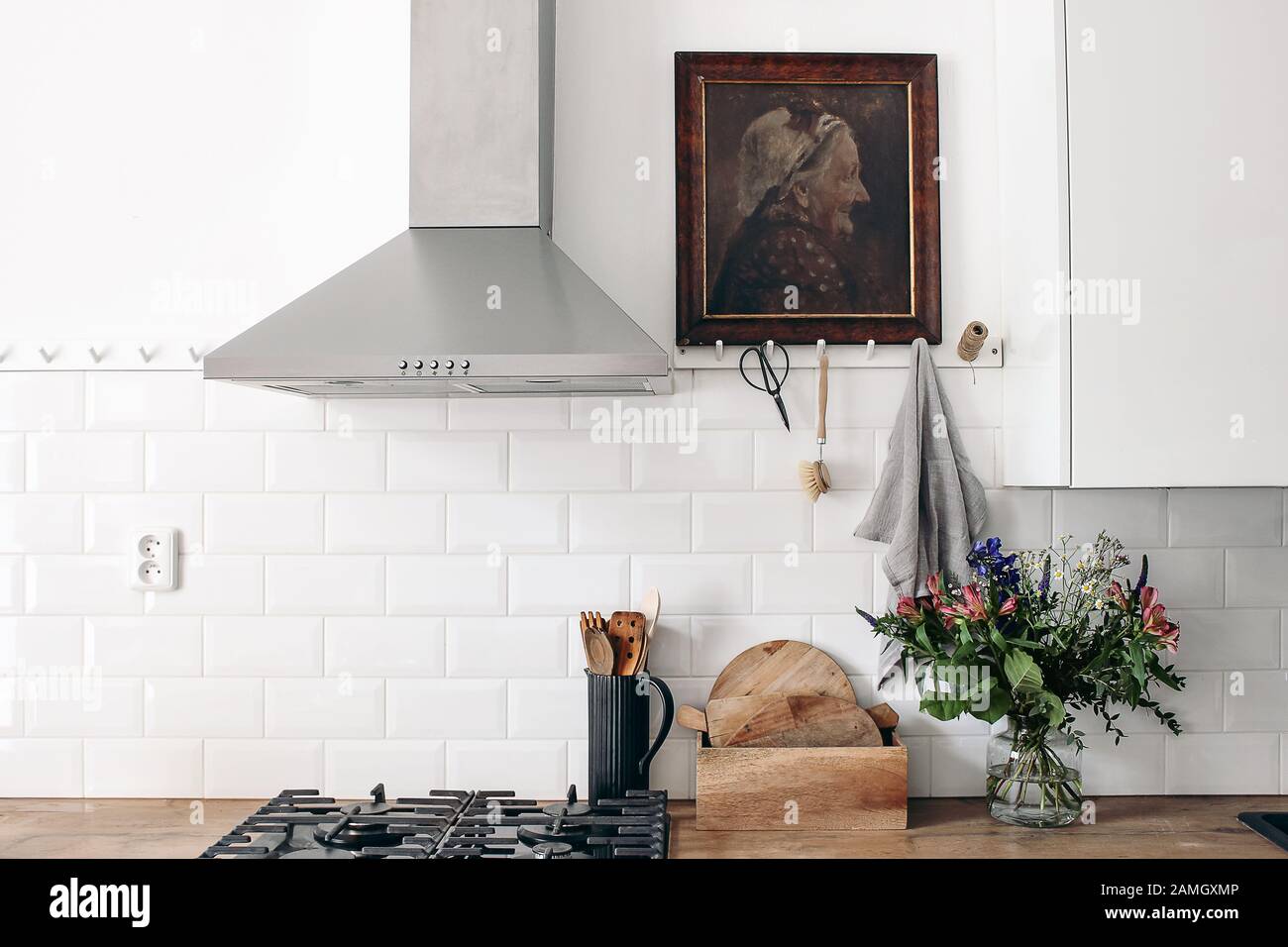 Modern eclectic kitchen interior. White brick wall with metro tiles, peg rails and oil painting. Wooden countertop, stainless steel hood and gas stove Stock Photo