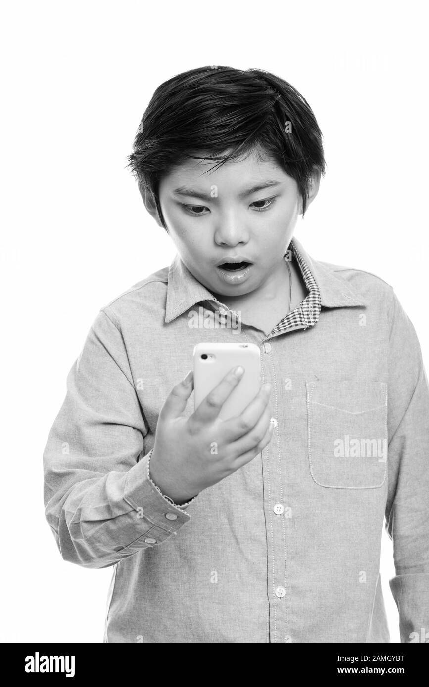 Studio shot of cute Japanese boy using mobile phone and looking shocked Stock Photo
