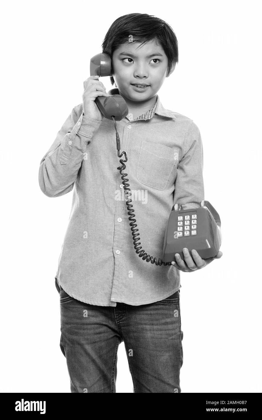 Studio shot of happy Japanese boy smiling and talking on old telephone Stock Photo