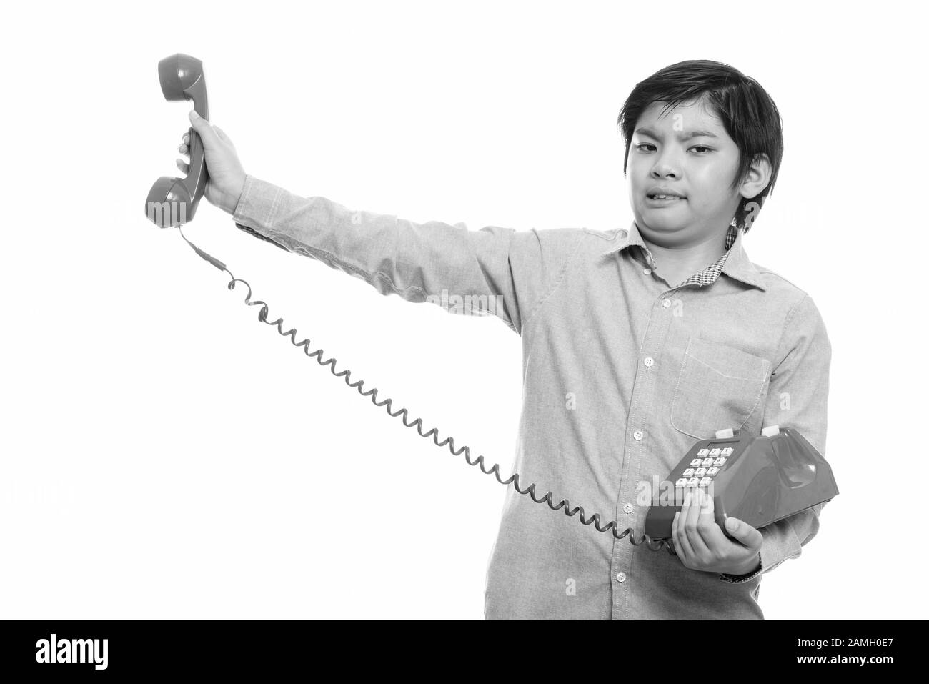 Studio shot of cute Japanese boy holding old telephone looking annoyed Stock Photo