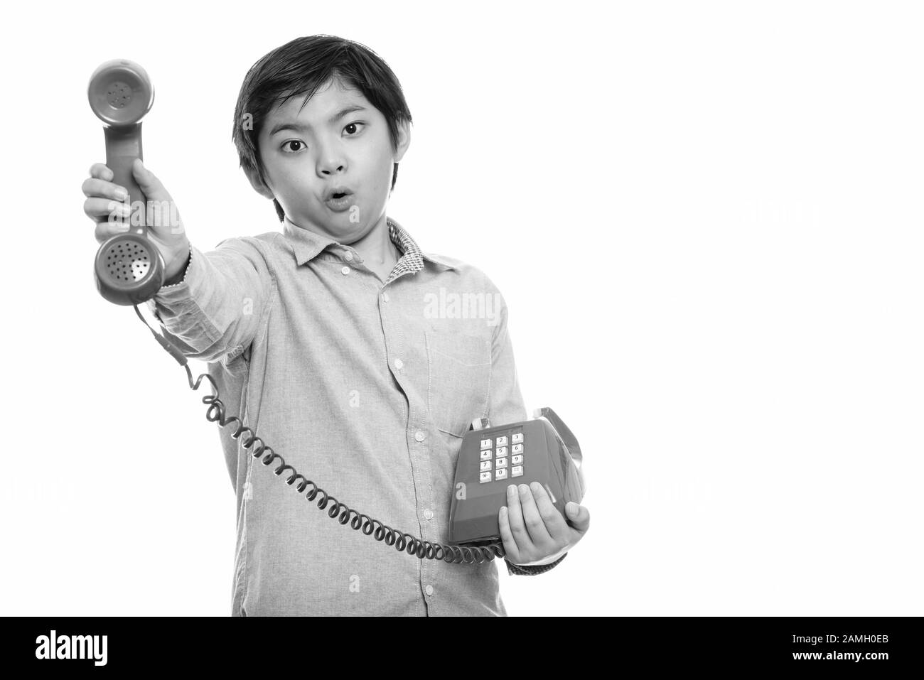 Studio shot of cute Japanese boy giving old telephone looking shocked Stock Photo