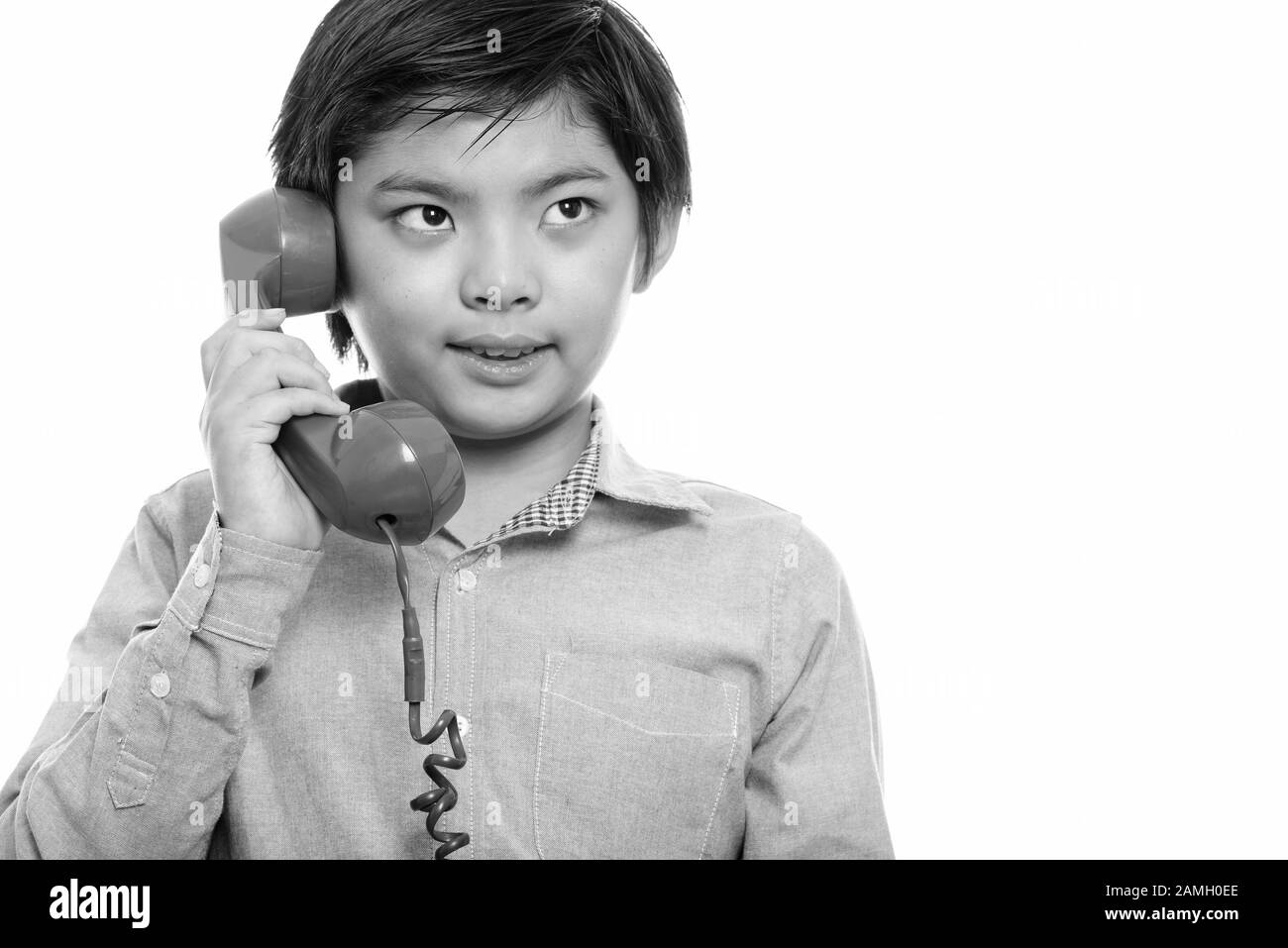 Studio shot of happy Japanese boy smiling and talking on old telephone Stock Photo